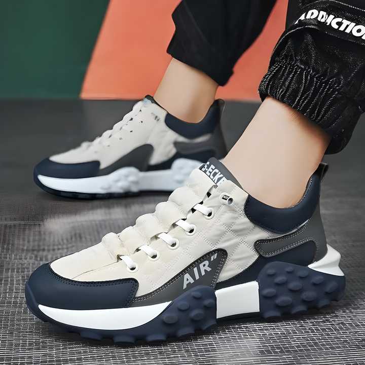 Gray and navy sneakers with white accents worn by a person on a textured floor.